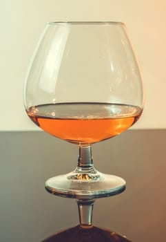 snifter of brandy in elegant typical cognac glass on light background, with reflection