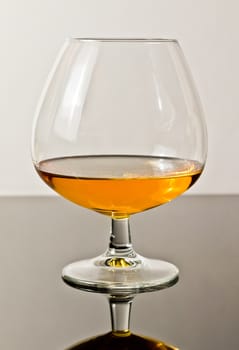 snifter of brandy in elegant typical cognac glass on white light background, with reflection