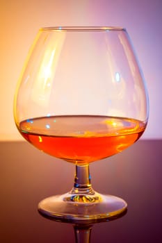 snifter of brandy in elegant typical cognac glass on colored light disco background, with reflection