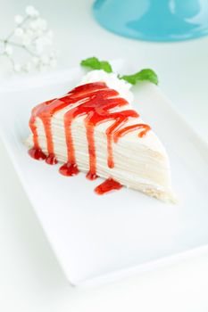 Fresh strawberry crepe cake slice with glaze drizzled perfectly and a mint garnish.