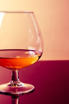 snifter of brandy in elegant typical cognac glass on purple colored light disco background, with reflection