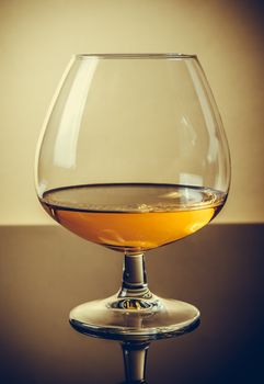 snifter of brandy in elegant typical cognac glass on old fashion style background, with reflection