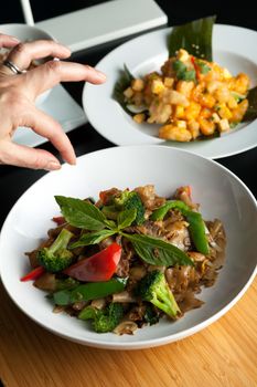 Food stylist grooms a dish by adding sweet basil garnish to the traditional thai dish Pad Kee Mao drunken noodle.