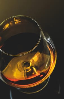 top of view of snifter of brandy in elegant typical cognac glass on dark background  with golden reflection, warm atmosphere