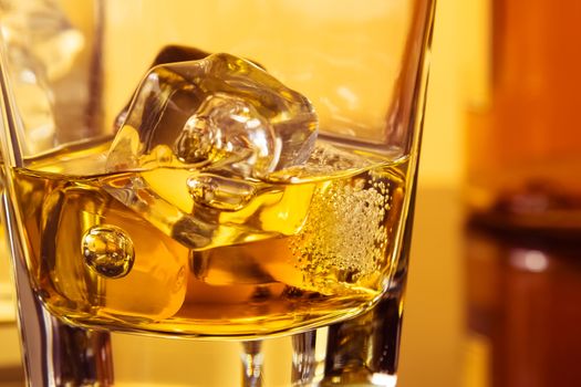 detail of glass of whiskey with ices near bottle on table with reflection, warm atmosphere, time of relax with whisky