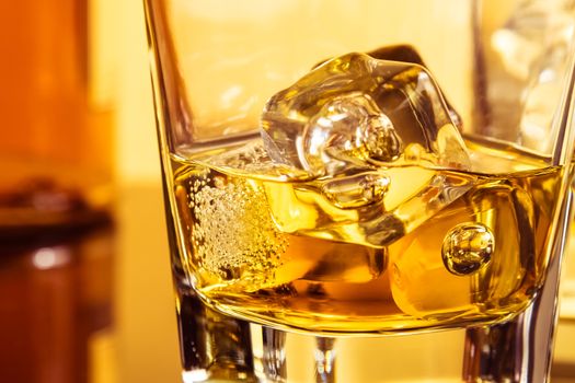 detail of glass of whiskey with ices near bottle on table with reflection, warm atmosphere, time of relax with whisky