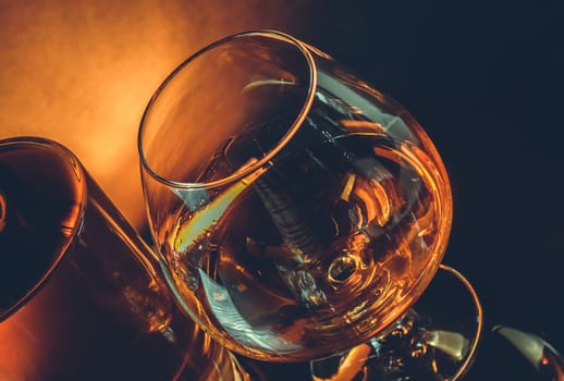 snifter of brandy in elegant typical cognac glass near bottle on black table warm tint style with space for text