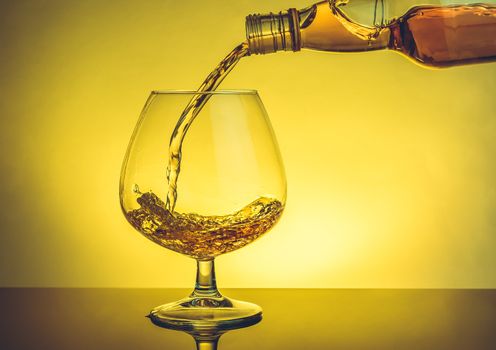 barman pouring snifter of brandy in elegant typical cognac glass on table on warm atmosphere