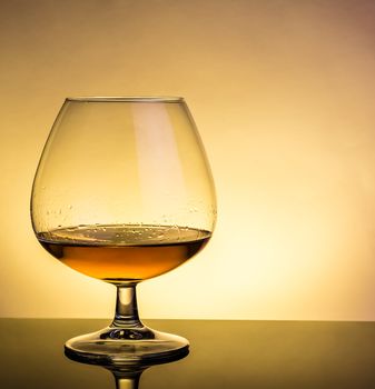 snifter of brandy in elegant typical cognac glass on table with reflection on warm atmosphere