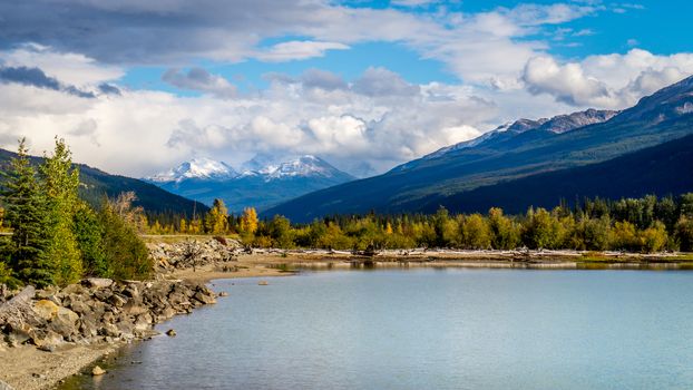 Moose Lake in Mount Robson Provincial Park in British Columbia, Canada under blue and partly cloudy sky. The mountains in the background are part of the Rocky Mountains