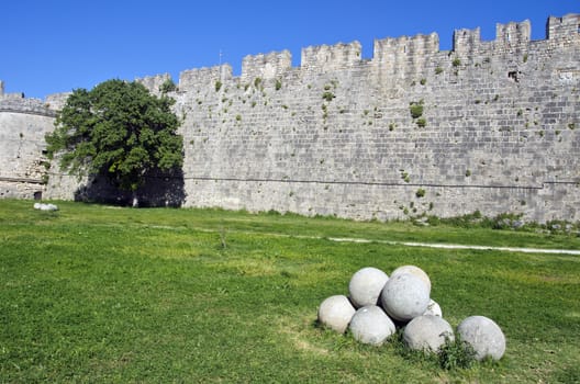 Stone wall, green tree and a pile of round stone objects in Greece