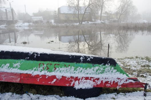 Upturned old wooden boat by river in winter time