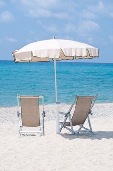 two deckchairs on the beach under an umbrella