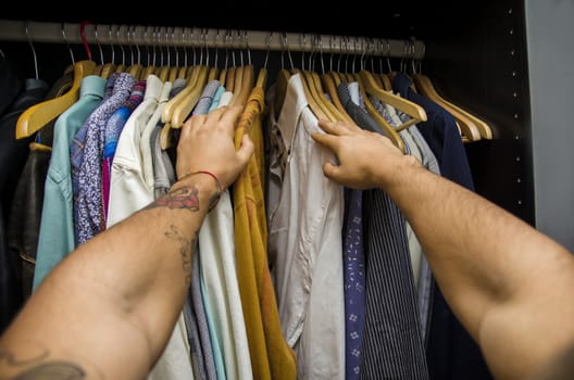 Man searching for a shirt hanging on the rail in his wardrobe, first person point of view looking down his arms. Self POV