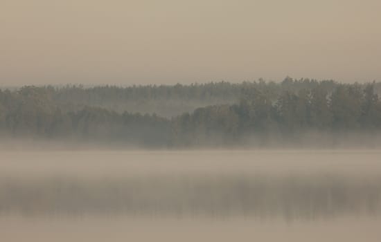 Poland.Bory Tucholskie National Park in autumn , august.Very dense, morning mist float over the lake and surrounding forests..Horizontal view.