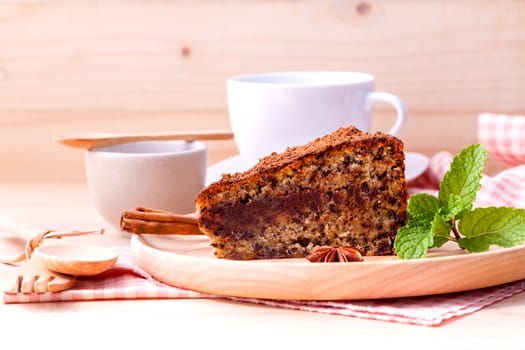 Homemade dark chocolate cake with cup of coffee on wooden background.