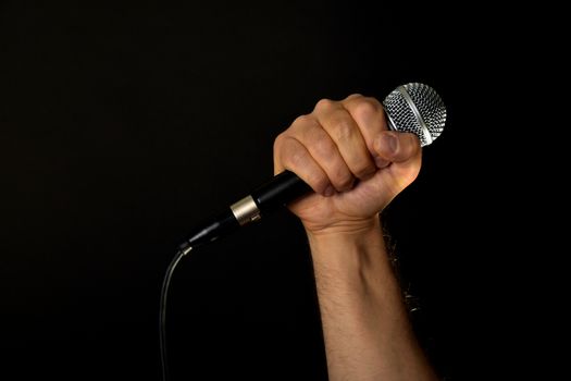 Male hand holding microphone with wire cable isolated on black background