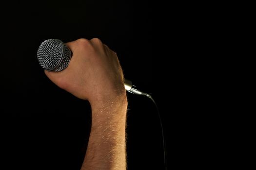 Male hand holding microphone with wire cable isolated on black background