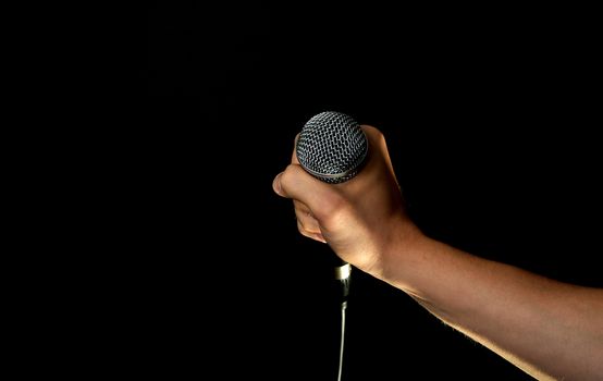 Male hand holding microphone with wire cable isolated on black background