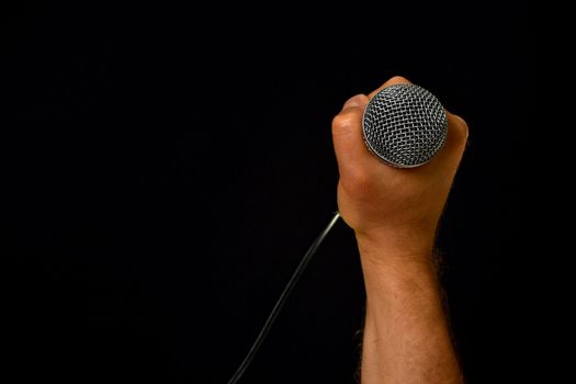 Male hand holding microphone with wire cable isolated on black background