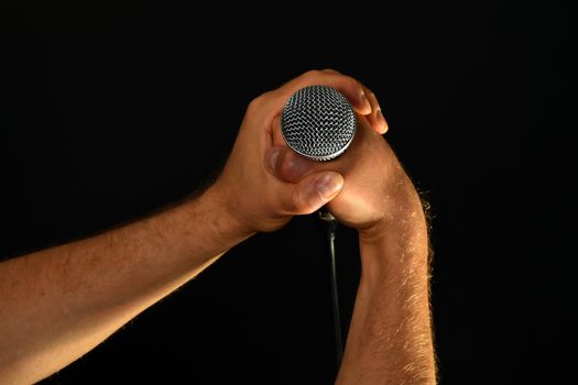 Two male hands holding microphone with wire cable isolated on black background