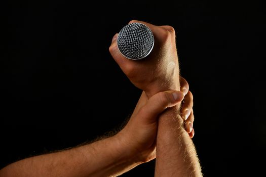 Two male hands holding microphone with wire cable isolated on black background