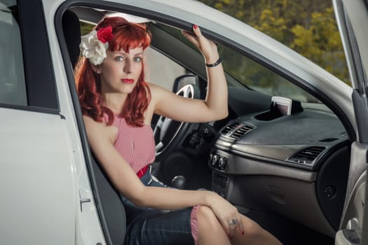 View of pinup young woman in vintage style clothing next to a white car.