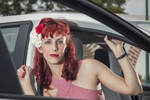 View of pinup young woman in vintage style clothing next to a white car.