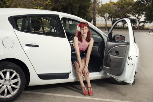 View of pinup young woman in vintage style clothing next to a white car.