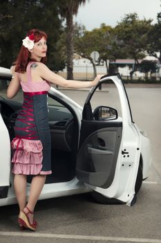 View of pinup young woman in vintage style clothing next to a white car.