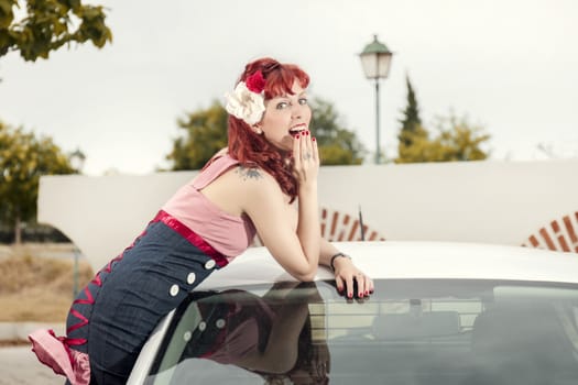 View of pinup young woman in vintage style clothing next to a white car.