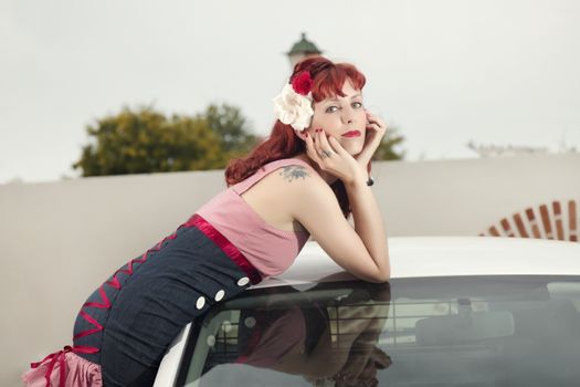 View of pinup young woman in vintage style clothing next to a white car.