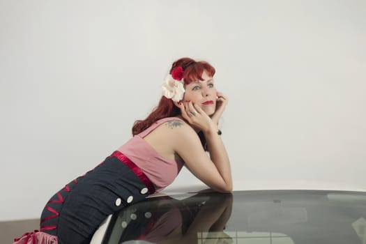 View of pinup young woman in vintage style clothing next to a white car.