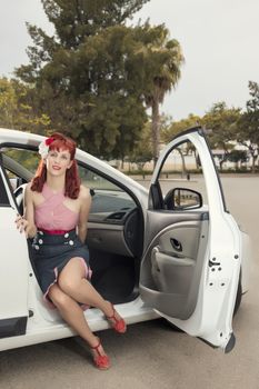 View of pinup young woman in vintage style clothing next to a white car.