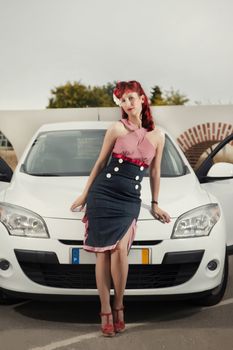 View of pinup young woman in vintage style clothing next to a white car.