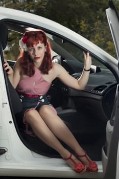 View of pinup young woman in vintage style clothing next to a white car.