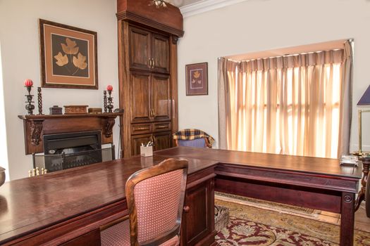 A private study in a residential home with wooden stydy table, chair, fireplace and cupboard in view near the winow.