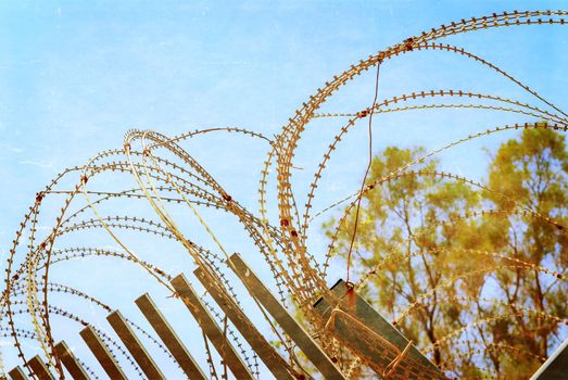 Security with a barbed wire fence with blue sky. Photo textured in old color image style.