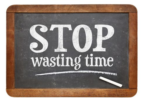 Stop wasting time sign - white chalk text on a vintage slate blackboard