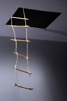 Escape concept. Rope ladder inside hatch in ceiling