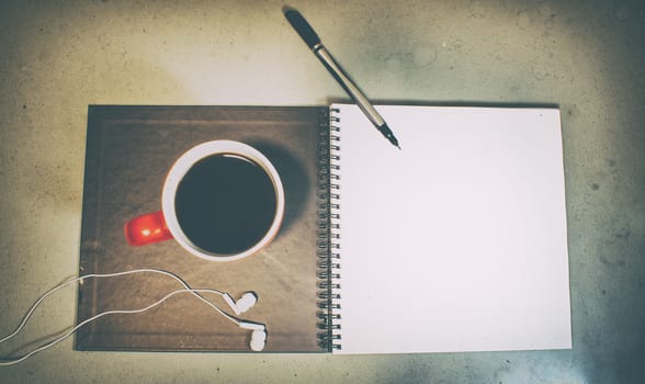 Photograph of an open notebook, a cup of soffee, a pen and a pair of earphones, with a grunge style
