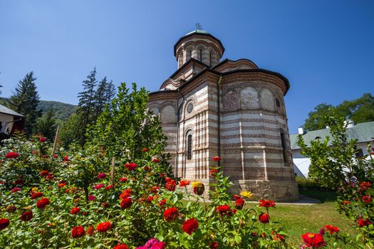 Cozia, Romania - Septemper 2, 2012: Cozia monastery church with red flowers on a sunny summer day, Romania