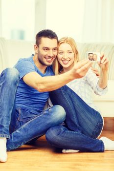 love, family, technology and happiness concept - smiling couple taking self portrait picture with digital camera at home