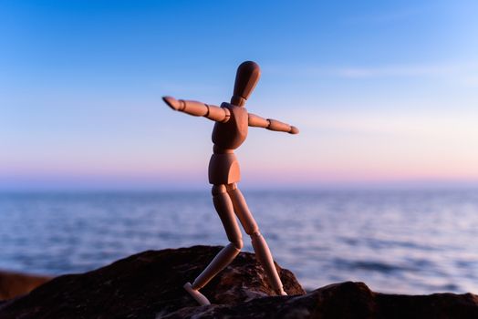 Wooden man stands on the top of sea boulder