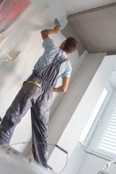 Thirty years old manual worker with wall plastering tools inside a house. Plasterer renovating indoor walls and ceilings with float and plaster.