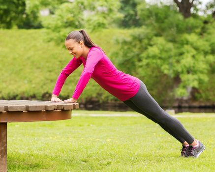 fitness, sport, training, park and lifestyle concept - smiling african american woman doing push-ups on bench outdoors