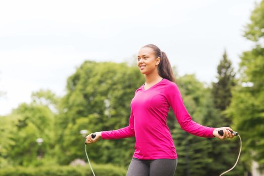 fitness, sport, training, park and lifestyle concept - smiling african american woman exercising with jump-rope outdoors