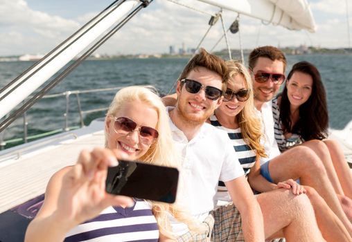 vacation, travel, sea, friendship and people concept - smiling friends sitting on yacht deck and making selfie