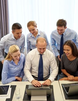 business, people, technology and teamwork concept - smiling business team with laptop computer working in office