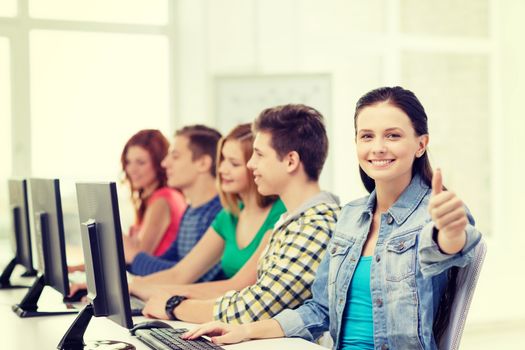 education, technology and school concept - smiling female student with classmates in computer class at school showing thumbs up